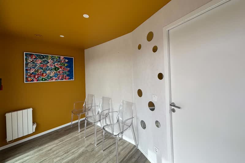 Salle d'attente : chaises transparentes, mur jaune et tableau de poissons colorés